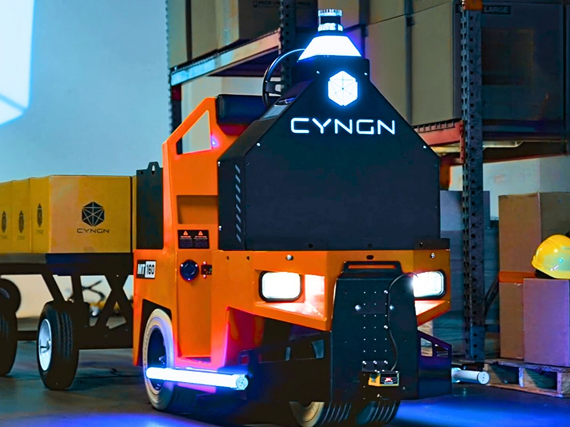 Cyngn DriveMod Tugger autonomous vehicle towing a loaded cart in a warehouse